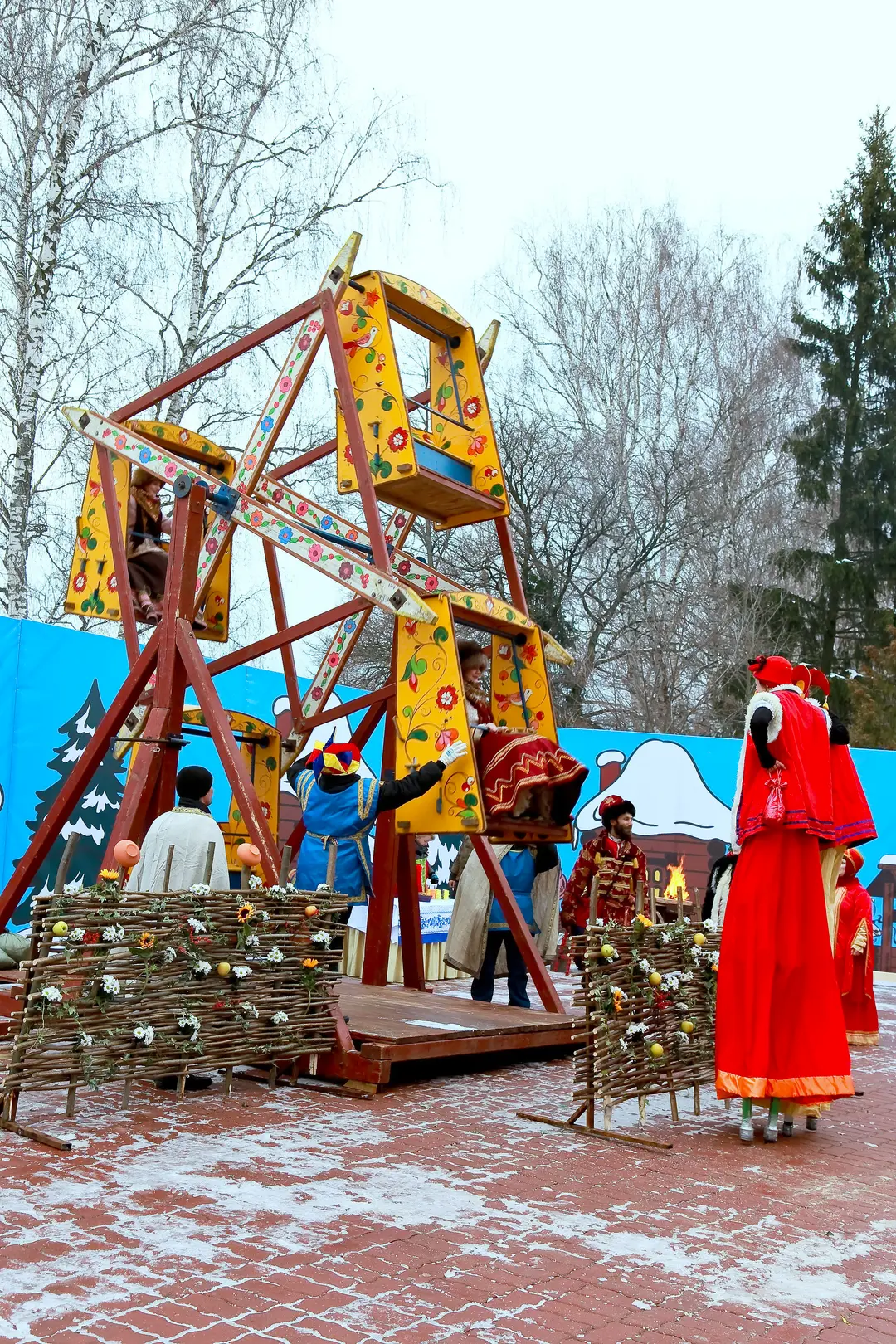Масленичный аттракцион-карусель в парке, ходулист в красном