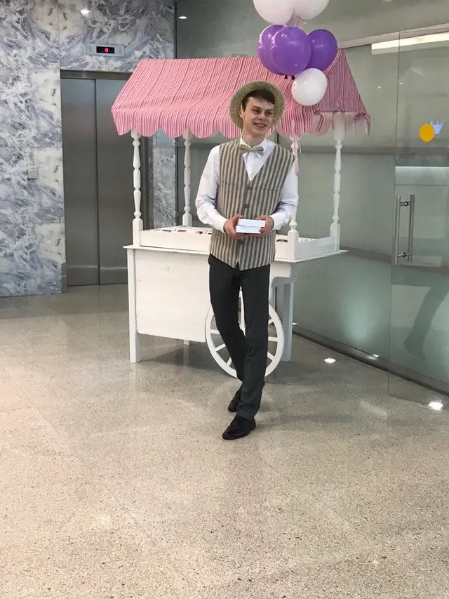 Промоутер в жилете и канотье у тележки Candy Land с шарами